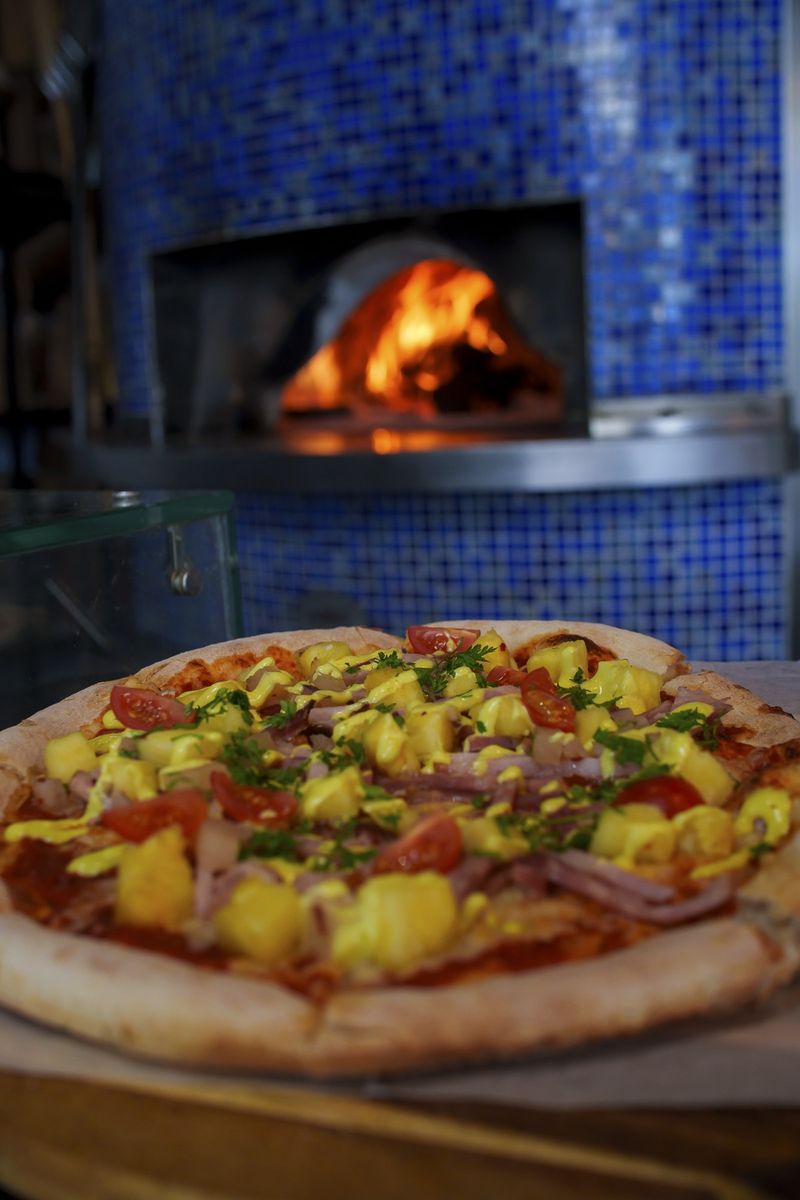 Ham di Pasku Pizza, the Christmas special at Pizzaliña Curaçao, in front of the blue-tiled pizza oven